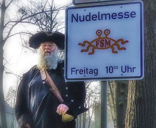 Ein Pastafari neben einem Hinweisschild für die Nudelmesse in Templin